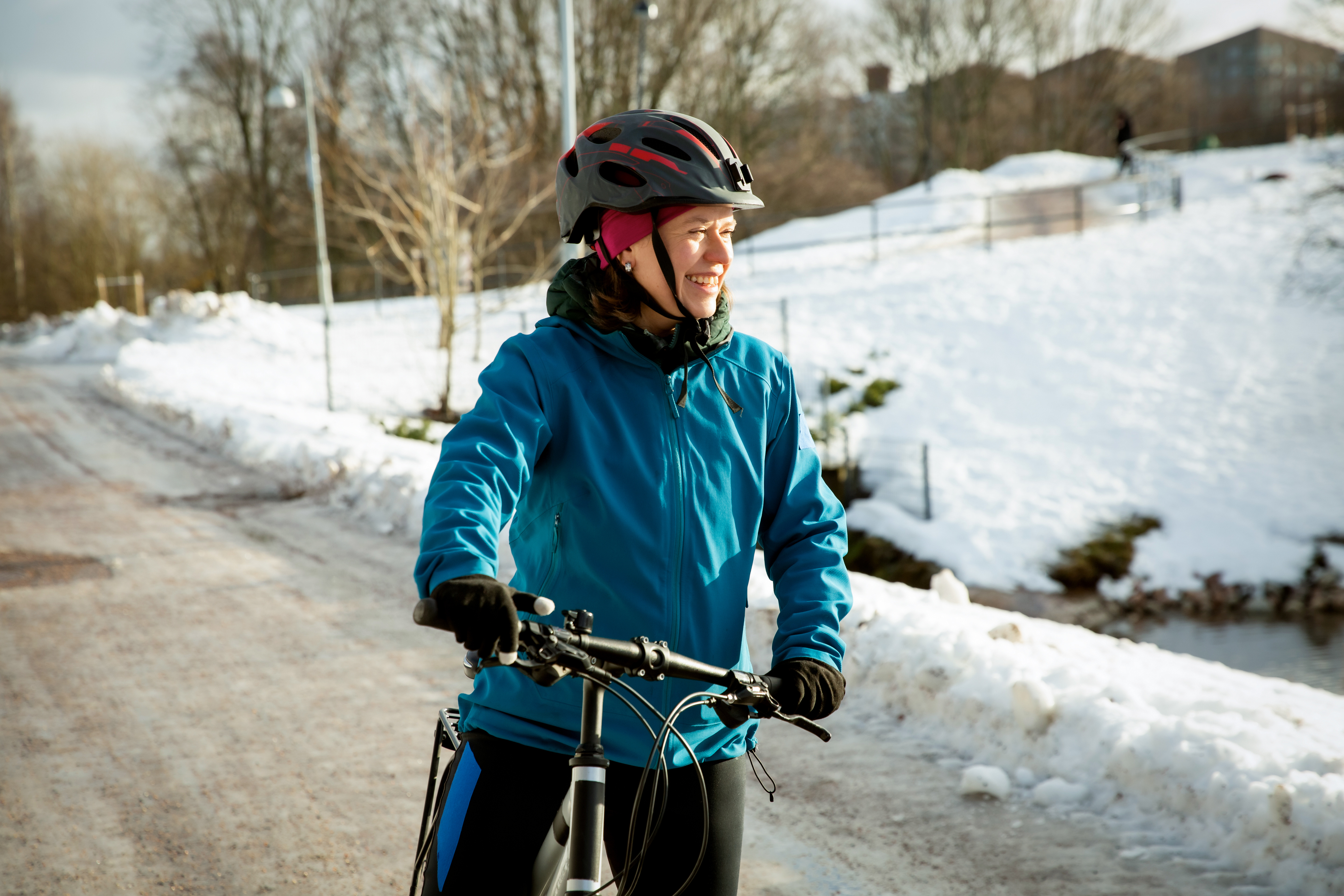 A smiling mid-adult woman stands with her bicycle on an icy path in a snowy Helsinki park, Finland, during winter commuting. High quality photo