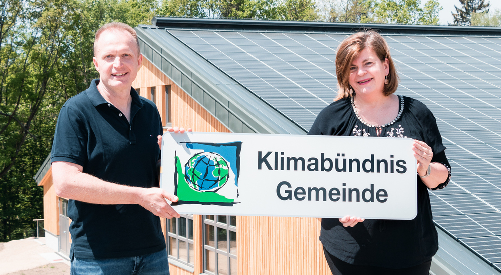 Johannes Heißenberger und Petra Schön halten die Klimabündnis-Tafel vor einer PV-Anlage.
