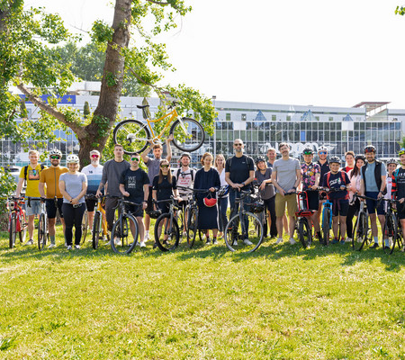 Ein Gruppe von Radler:innen stehen in Radkleidung und mit Rädern für ein Gruppenfoto zusammen.