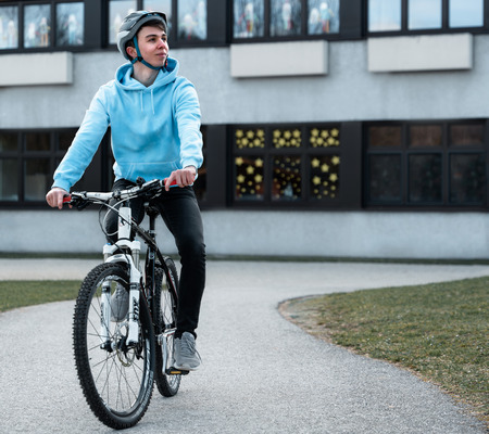 Jugendlicher fährt von der Schule mit Fahrrad weg.