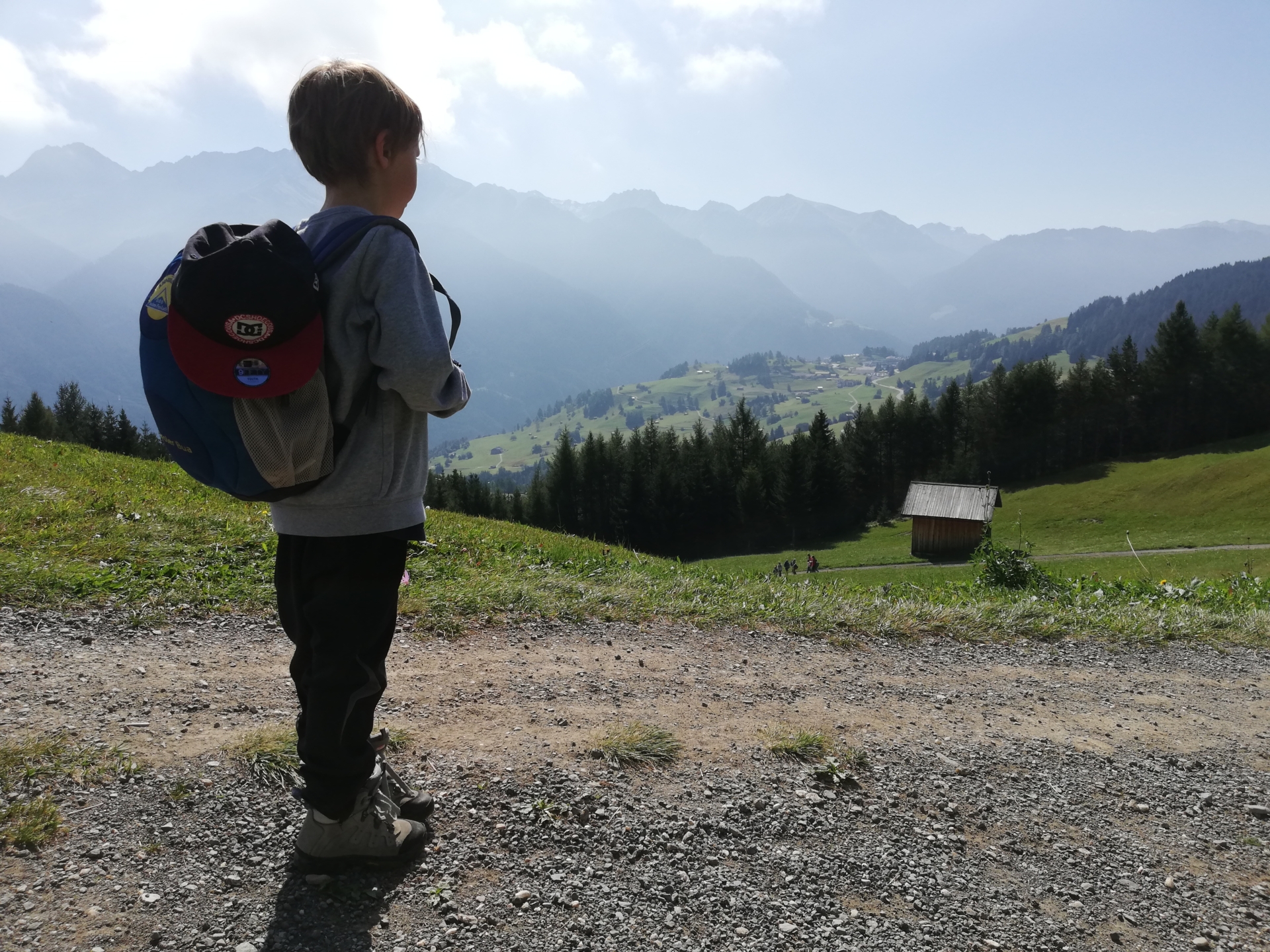 Kind mit Schultasche schaut auf Dorf im Tal