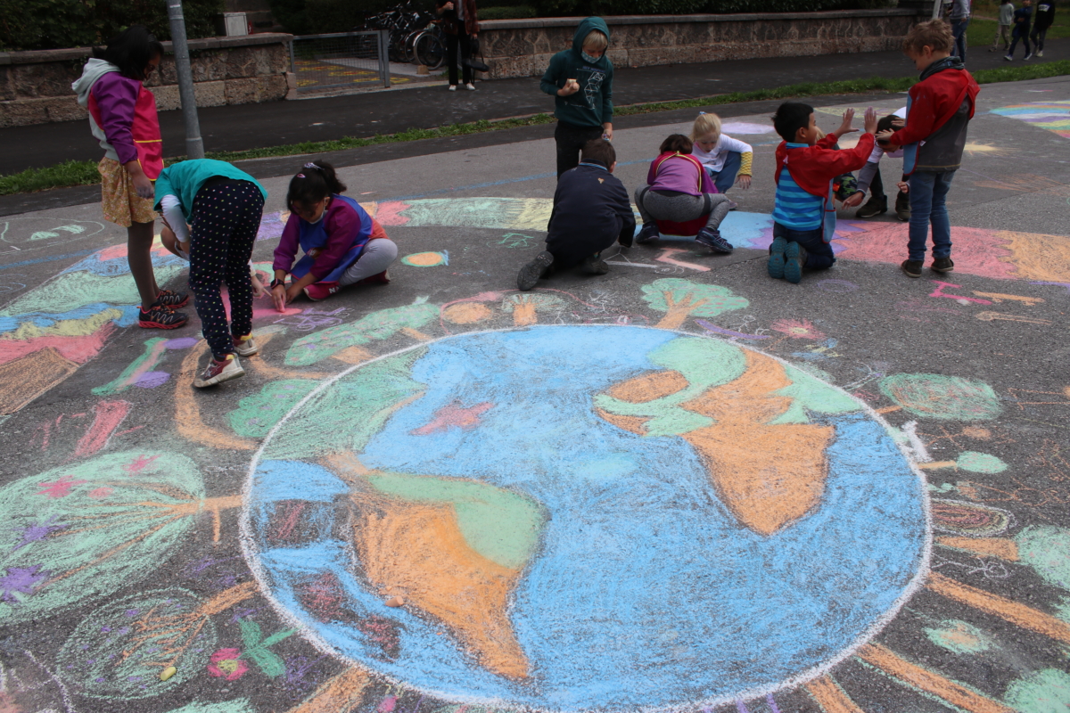 Kinder malen Weltkugel mit Kreide auf Straße