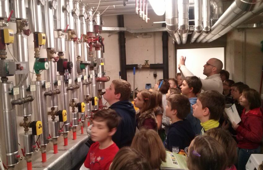 Kinder schauen auf Leitungen, die sich in einem Keller an der Wand befinden