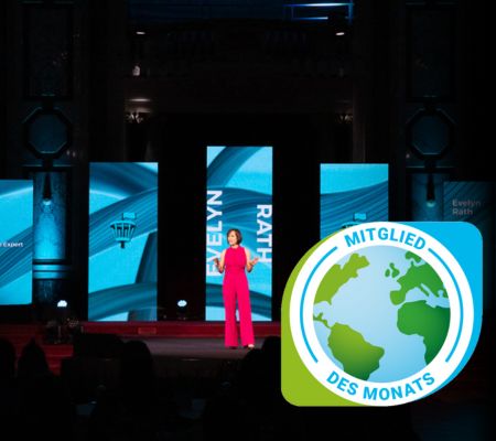 Evelyn Rath in pinken Anzug auf der Bühne, im Hintergrund hochformatige Screen mit blauem Hintergrund und ihrem Namen.