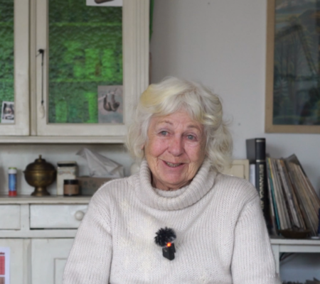 Eine ältere Dame sitzt im Wohnzimmer und lacht in die Kamera