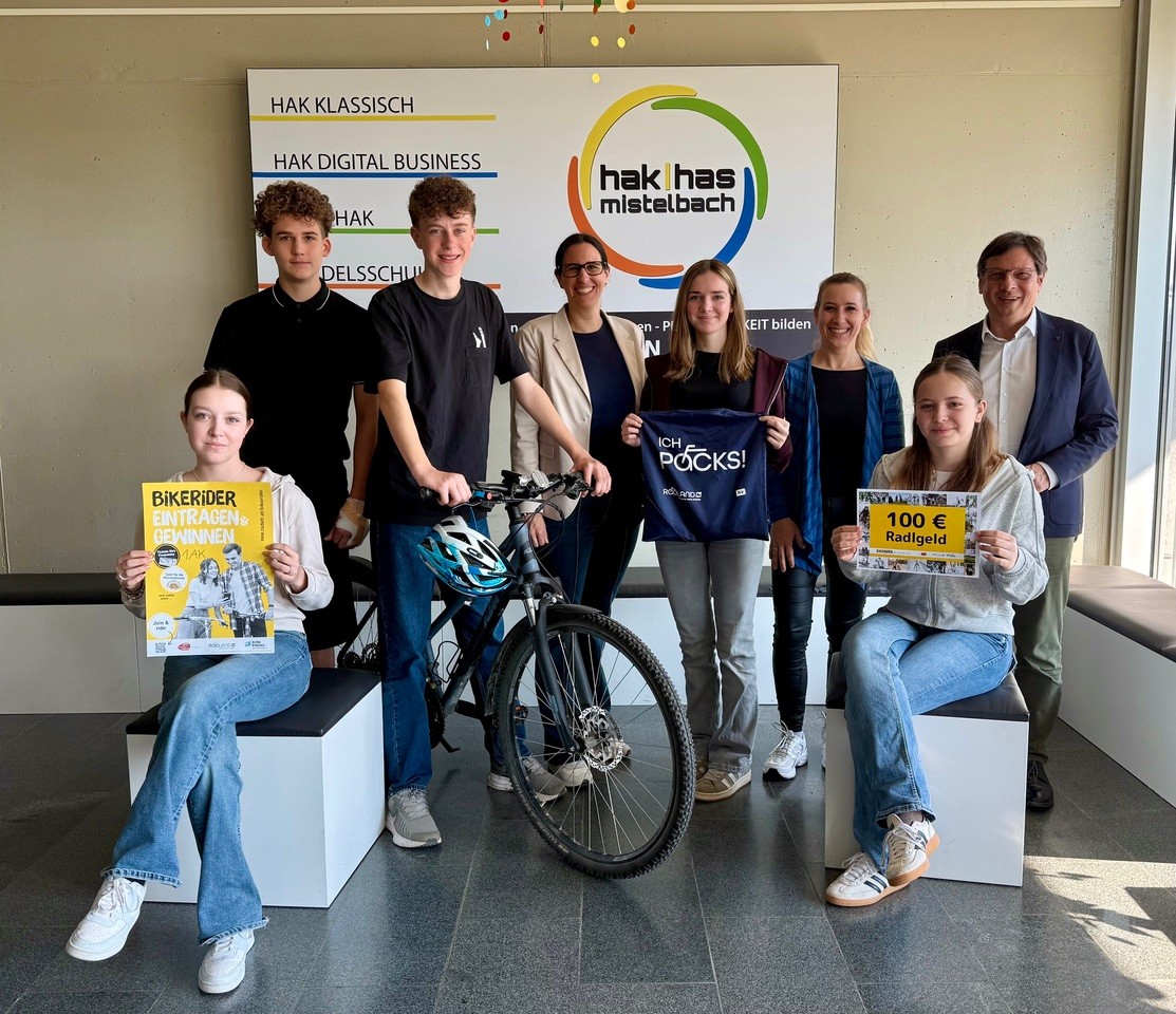 Gruppenfoto der fünf erfolgreichen Bikerider mit dem Schulleiter und der Schulleiter Stellvertreterin. Sie halten das Schild mit den 100 Euro Radlgeld in die Kamera und posieren mit einem Rad und Helm.