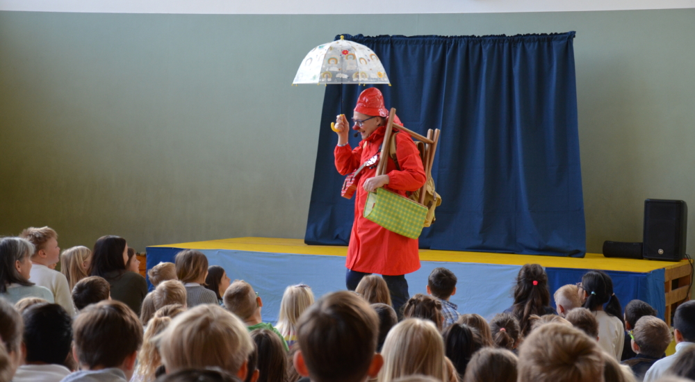 Klimaclown Dudu mit einem Regenschirm in der Hand geht ins Publikum