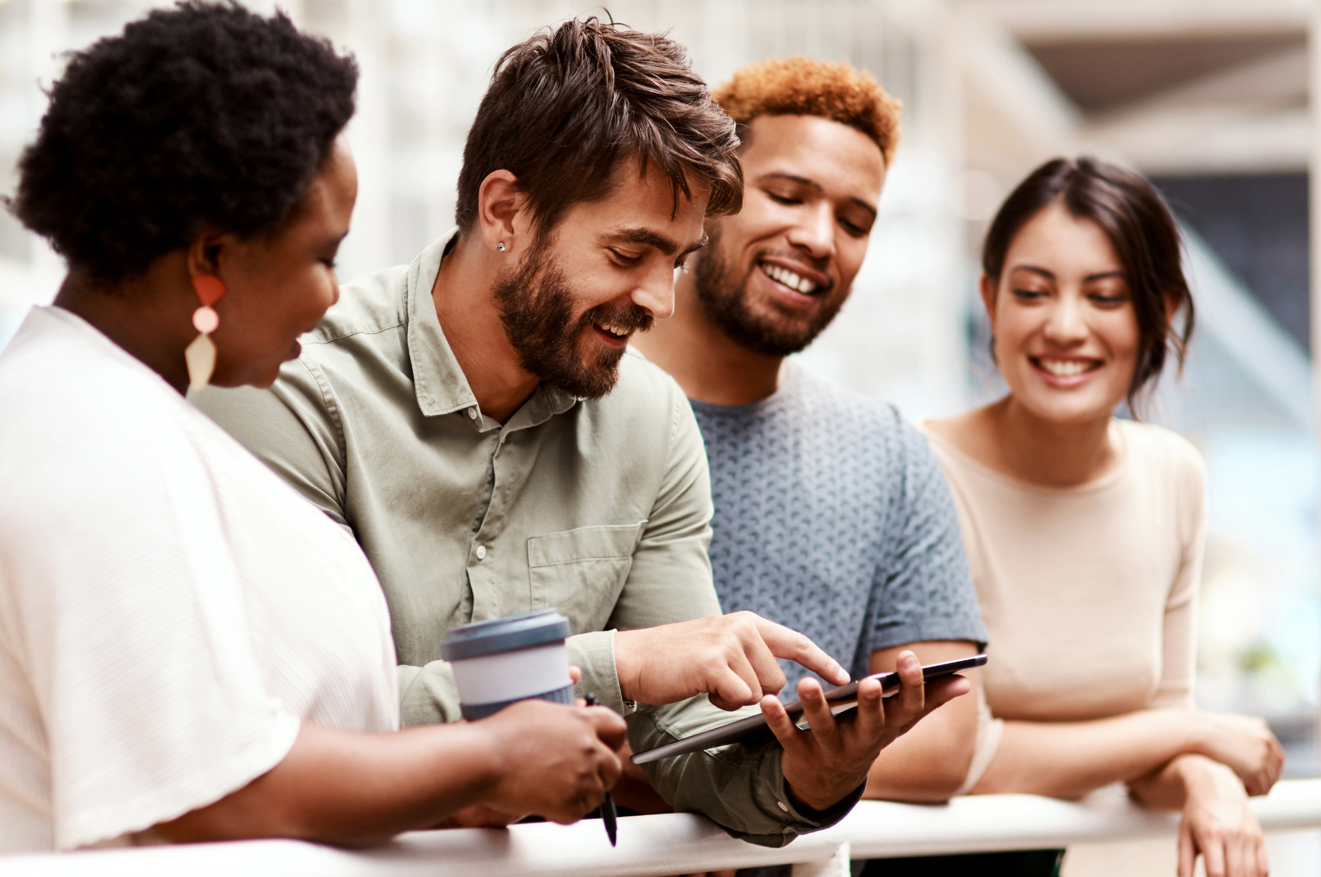 Vier junge Menschen lachen und schauen gemeinsam auf ein Tablet